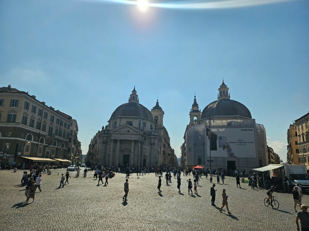 Wide view of Piazza del Popolo with twin domed churches and cobblestones